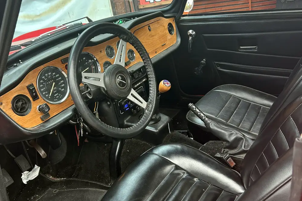The wood dashboard of a 1976 Triumph, with a modern head unit fitted in the console